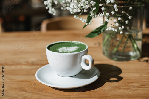 Matcha latte hot drink on a wooden table next to a bouquet of flowers in a vase.