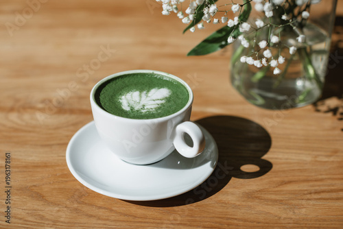 Matcha latte hot drink on a wooden table next to a bouquet of flowers in a vase.