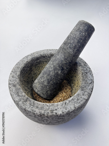 Fotografie Angled view of stone mortar and pestle with cumin seeds on white background