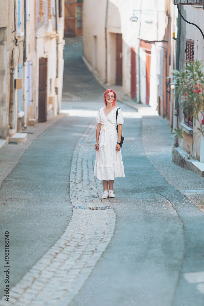 Obraz premium A traveler strolls through a picturesque alley in a quaint village in Provence, France. The charming white buildings and cobblestone paths create a dreamlike atmosphere perfect for exploration