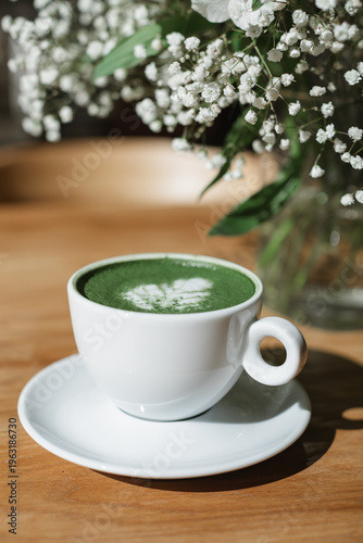 Matcha latte hot drink on a wooden table next to a bouquet of flowers in a vase.