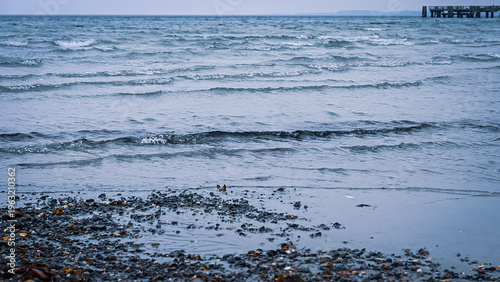 Foto Waves hitting a pebbly part of the beach under a cloudy sky, a view across the b