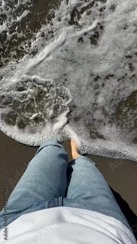 Video of bare feet standing on a sandy beach as gentle waves approach. The scene evokes a sense of relaxation and connection with nature, highlighting the serene beach atmosphere.