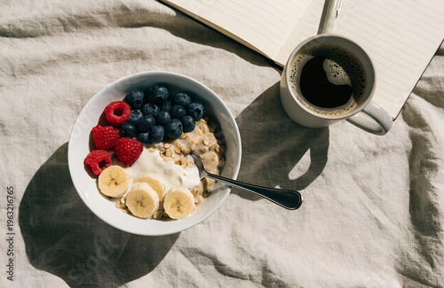 Healthy Breakfast: A bowl of oatmeal with fresh berries and sliced bananas sits alongside a cup of coffee and a notebook, creating a scene of wholesome nourishment. 