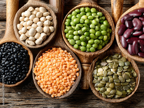 Variety of vegan protein ingredients including tofu, tempeh, beans, lentils, nuts, and seeds on rustic wooden, healthy display.