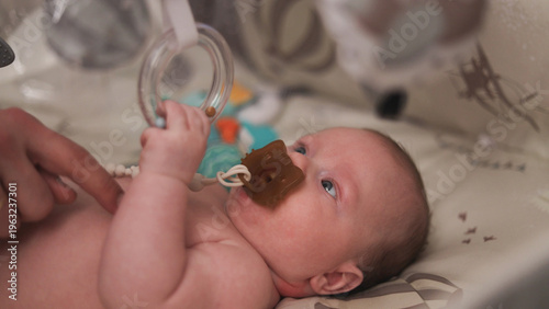 Fotografie Close-up of a baby's face with a pacifier and a parent's hand gently touching th