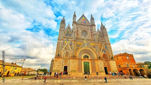 Quadro su tela Magnificent Gothic Facade of Orvieto Cathedral (Duomo di Orvieto) with golden Mosaics and tourists under cloudy blue sky