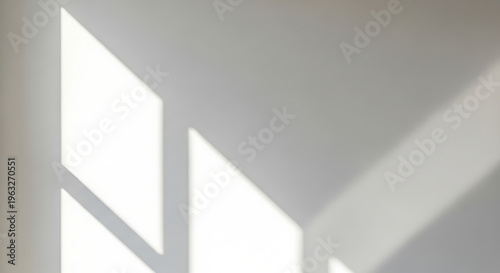 Abstract geometric patterns of natural sunlight cast dynamic shadows across a clean white wall, creating a serene and minimalist aesthetic in a bright indoor setting