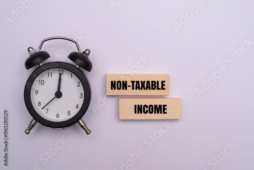 Tableau sur toile An alarm clock next to wooden blocks with text NON-TAXABLE INCOME on a white background