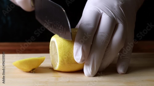 A cook cuts a lemon into wedges with a knife on a wooden board. Close-up.
