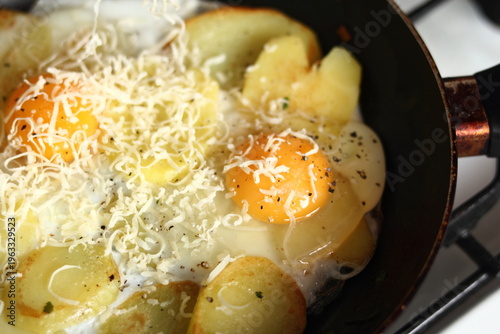 Making sunny side up eggs with fried potato and grated cheese