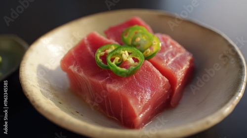 A ceramic plate with fresh sashimi slices, garnished with green chili rings, minimalist presentation. menu design.