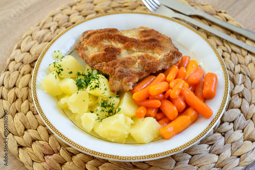 Fried pork neck cutlet in breadcrumbs, served with boiled potatoes and baby carrots