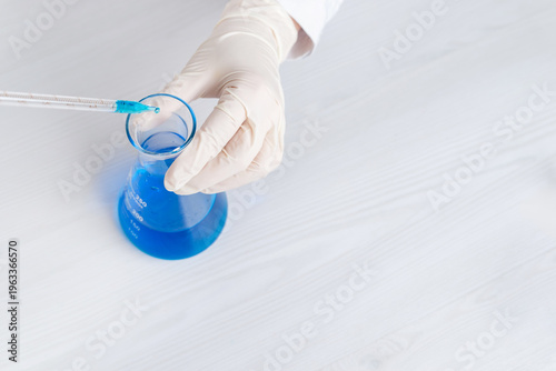 Obraz na plátně Top view of pipette adding blue liquid into laboratory flask, chemical experimen