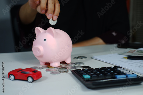 Putting coins in a piggy bank, miniature cars on the office desk, planning and calculating to save, visualizing planning to buy a new car, dream visualization, financing
