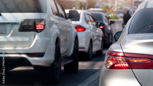 Rear side of cars driving on the asphalt road. Turn on brake light by traffic jam in the business time. Blurred background of the town at day in Thailand.