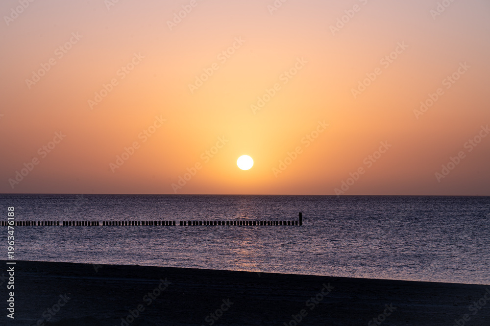 Obraz premium A peaceful sunrise at the sea with warm, vibrant colors and a tranquil horizon; wooden groyne for coastal protection on the south beach of 23775 Großenbrode, Baltic Sea, Germany