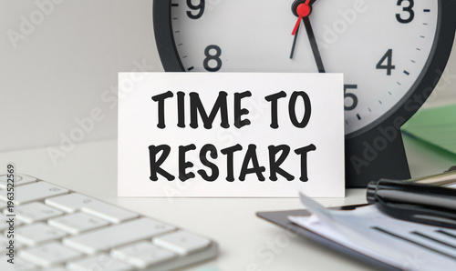 Time To Restart text on a white card standing on an office desk with a clock and keyboard, symbolizing fresh starts and business recovery.