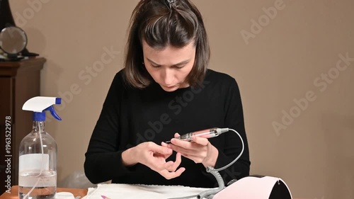 Young woman doing electric manicure with nail drill at home