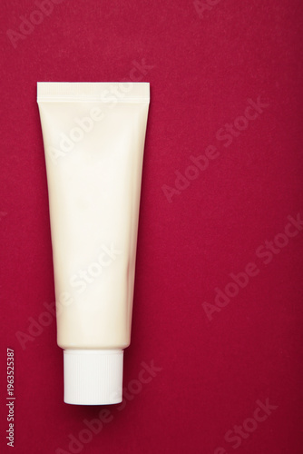 Canvastavla Beige tube of cream on dark red background