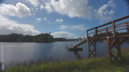 Clouds move across blue sky by lake and dock.