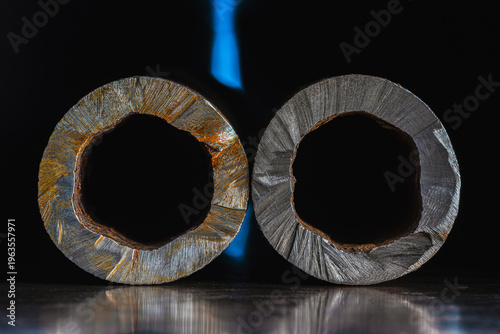 Close up of the cross section of an old rolled metal pipe with irregular walls, showing detailed cut metal texture in an industrial setting