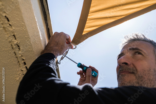 Middle-aged man installing a sail shade on a building's terrace.
DIY, lifestyle, people, home life