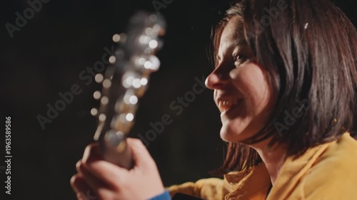 Happy woman strumming. Joyful woman practicing guitar outdoors. Smiling female musician enjoying cord practice outside. Cheerful woman in camping setting tuning her acoustic guitar