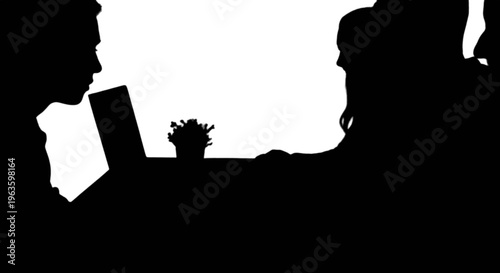 Silhouette of two people interacting with a laptop