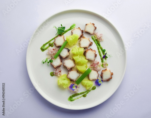 Artfully plated, deconstructed octopus salad. Sliced tentacles with vibrant green potatoes, shallots, a rich pesto drizzle, and edible flowers on minimalist white ceramic.