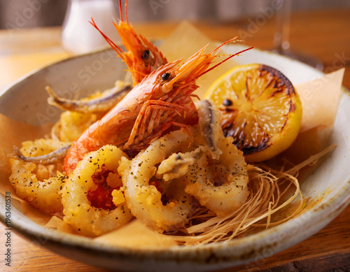 Golden Fritto Misto featuring crispy calamari rings, whole shrimp, and small fish. Served with a charred lemon half and garnished with aromatic herbs.