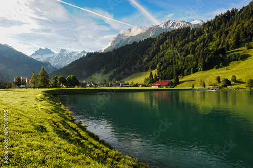 Cuadro en lienzo Sunlit Alpine Pasture and Red Barn by a Clear Mountain Lake in Engelberg