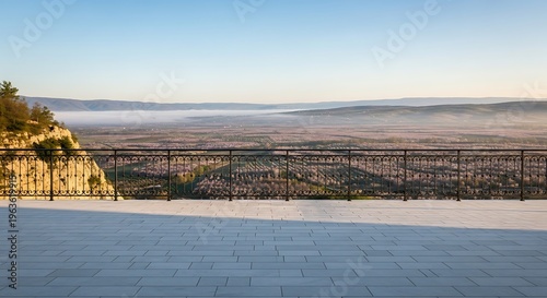 Panoramic view of a misty valley at sunrise from a stone terrace with an ornate railing