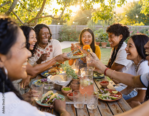 A group of diverse friends shares delicious Mexican tacos and salsa at a garden wooden table during the golden hour.