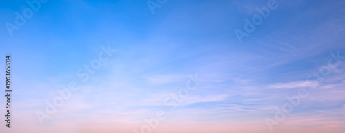 Wide-angle view of serene sky, soft blue gradient fading to pink horizon. Gentle wisps of cloud stretch across calm expanse. Ideal for backgrounds, travel