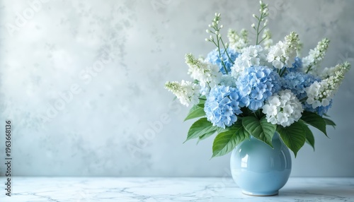 Blue and white hydrangea bouquet in light blue vase. Soft floral arrangement with green leaves on marbled surface. Pastel decor for home interior.