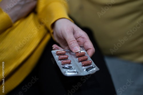 Close-up of a person holding a blister pack of red capsules, medication and healthcare concept, pharmaceutical treatment, daily medicine intake, pain relief or antibiotics.