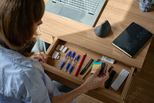 Tableau sur toile Woman holding sticky note pad over open desk drawer with office supplies near la