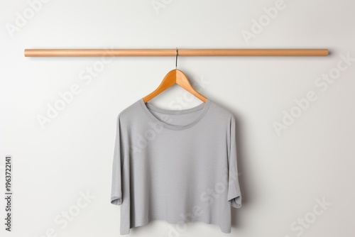 Simple gray t shirt hanging on a natural wood clothes rod against a white wall