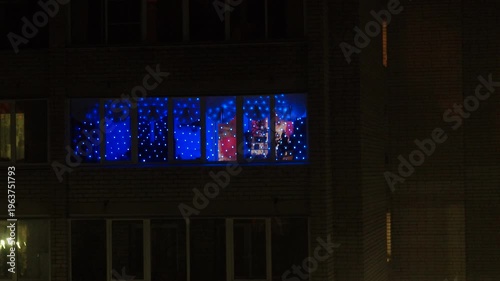 Night view of the balcony or lodge opposite. Colorful winter lights twinkle in warm city setting, creating a magical atmosphere. Soft snow blankets the ground, enhancing the festive spirit of dark.