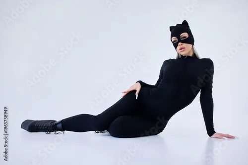 Fototapeta samoprzylepna Confident woman in feline costume. Female model in black bodysuit with cat accessories. Stylish female model poses confidently in feline themed outfit with glamourous lighting
