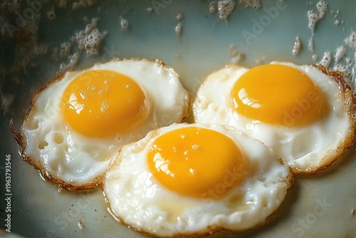Three sunny-side-up eggs frying in a pan with glossy golden yolks and crisp browned edges, warm and appetizing breakfast
