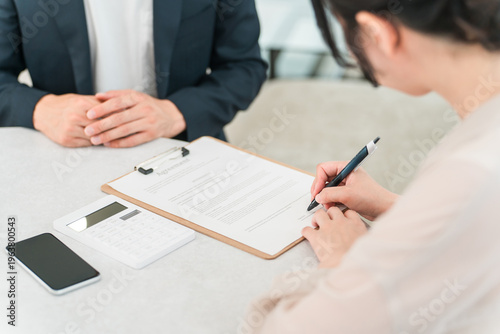 Obraz na płótnie A female client signing a contract, pledge, and consent form, while a male businessman explains the process