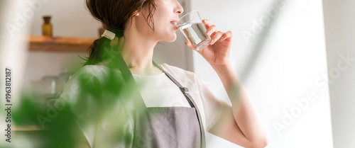 Foto A woman in an apron drinking water from a glass in the kitchen (hydration, miner
