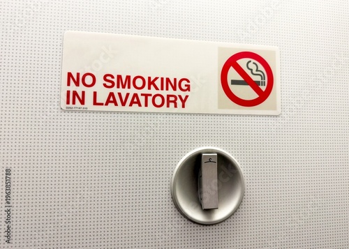 Airplane Lavatory No Smoking Sign, CloseUp Showing Wall Decal And Rotary Latch, Textured White Panel, Bold Red Prohibition Symbol, Travel Safety Compliance And Cabin Maintenance