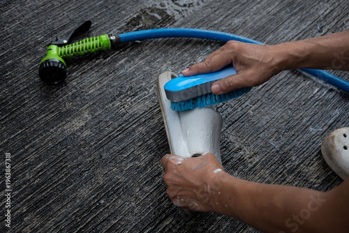 people washing rubber slippers with water hose and plastic brush, cleaning on house yard, natural background