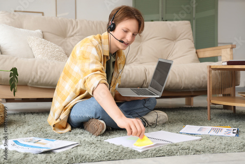 Teenage boy with laptop, headset, charts and notebook working online at home