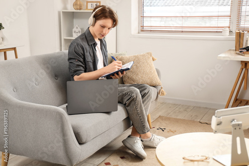 Teenage boy with laptop, headphones and notebook working online at home