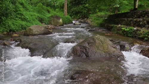 Clear river flow with refreshing scenery, showing crystal water, natural stones, and calming atmosphere in a serene tropical landscape