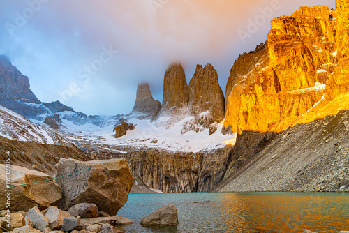 Fotografi The iconic three granite towers of Torres del Paine glowing in golden morning light above a turquoise glacial lake at the Base of the Towers lookout